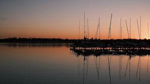Un lac paisible où plusieurs bateaux sont amarrés à un quai au coucher du soleil.