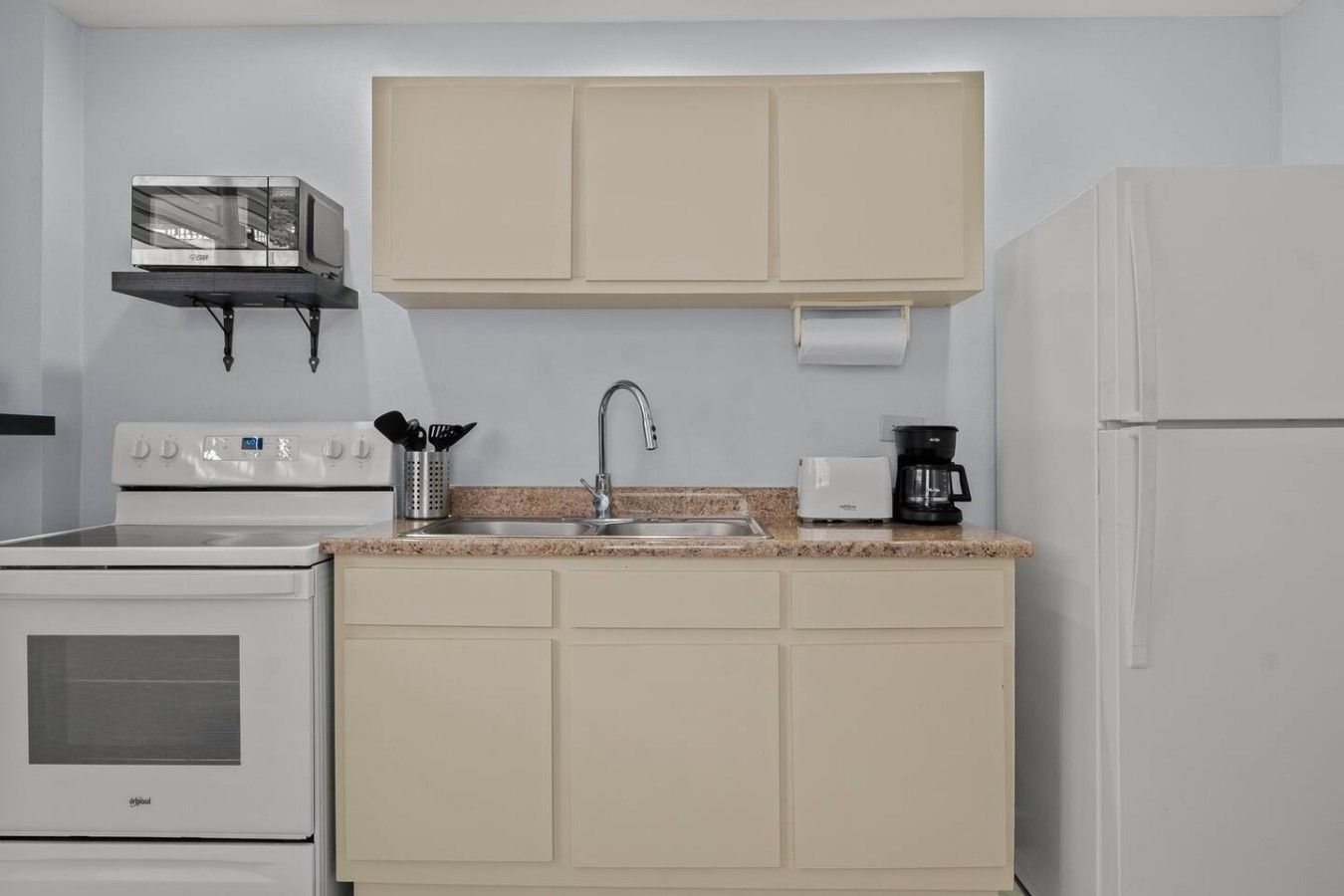 Una cocina compacta con estufa, lavamanos y cafetera.