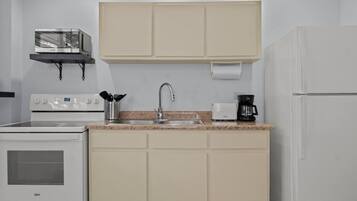 Una cocina compacta con estufa, lavamanos y cafetera.