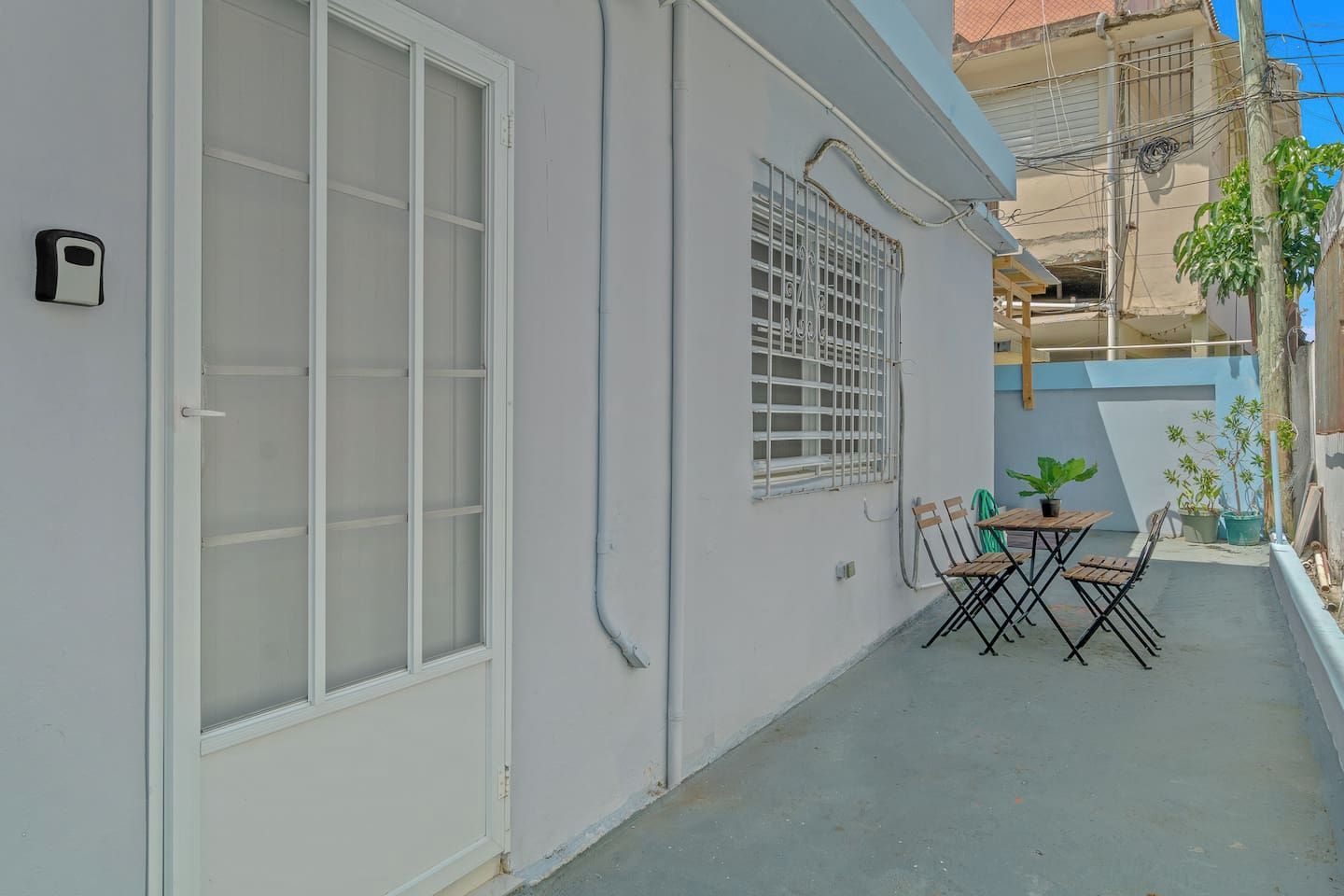 A residential building with a large window, a door, and a small patio area with a table and chairs.