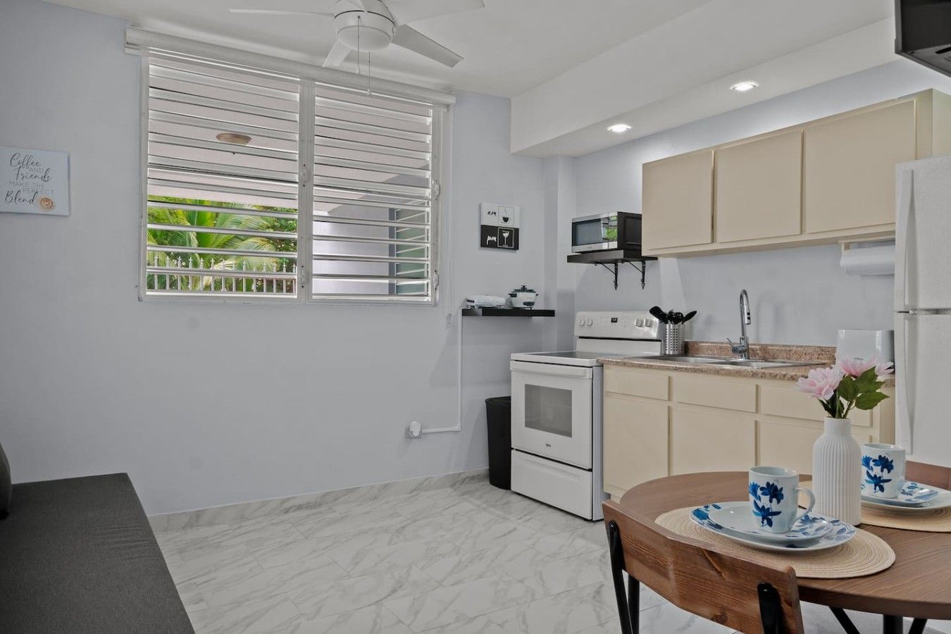 A modern kitchen with a stove, oven, and microwave. There is a dining table with a vase and a cup.