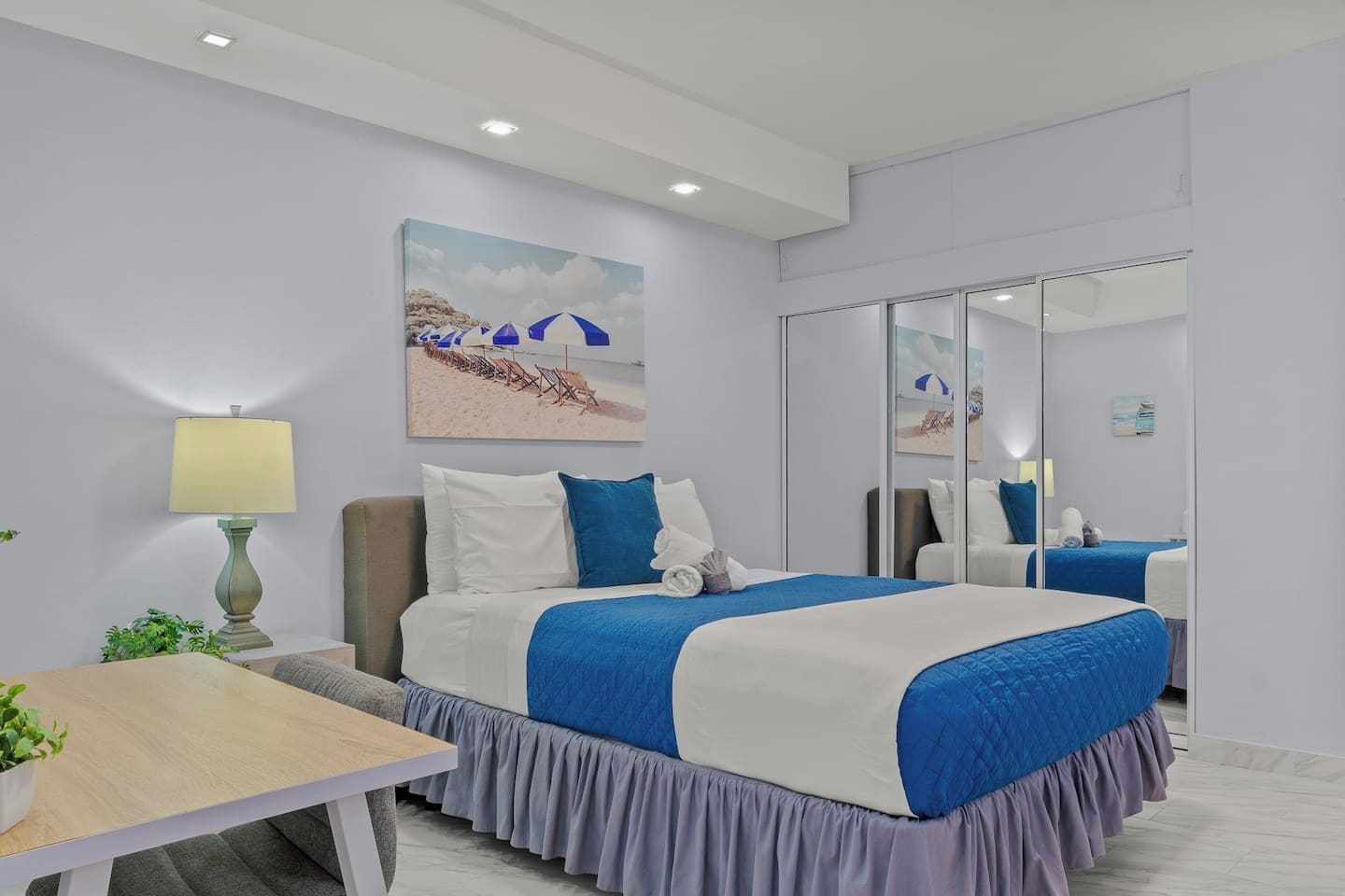 A hotel room with a bed, bedside table, lamp, and a painting on the wall.