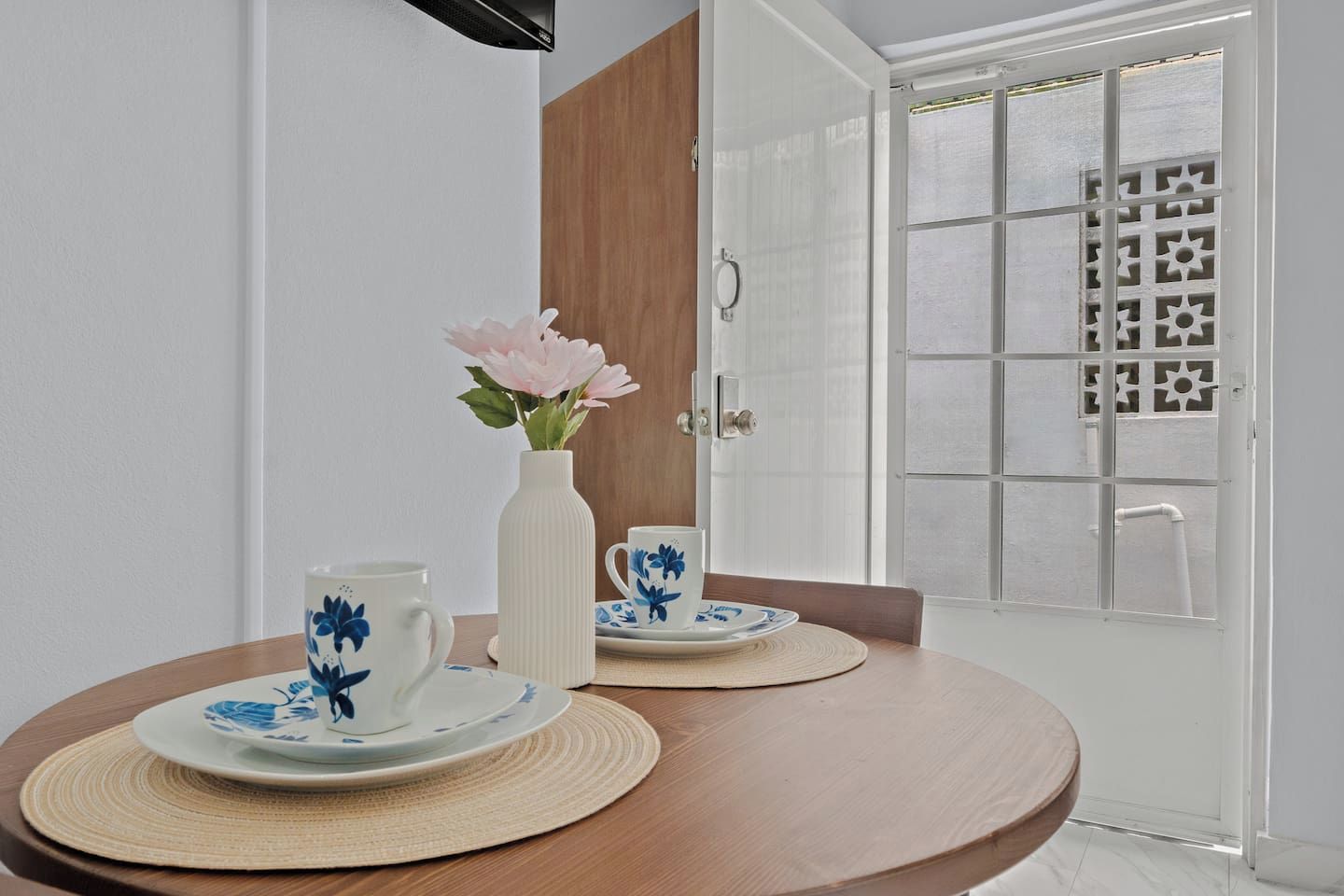 A dining table with two plates and cups, a vase with flowers, and a door with a patterned window.