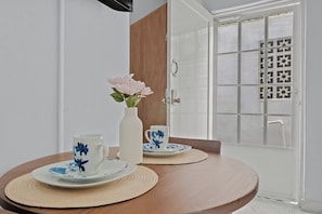 Una mesa de comedor con dos platos y tazas, un florero con flores, y una puerta con un ventanal decorado.