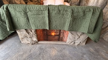 Una habitación con chimenea de piedra, una colcha verde acolchada sobre ella y una pared de ladrillo.