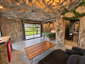 A room with a stone wall, a bed, a wooden table, a sofa, and a bathroom with a brick wall. - Quartz Cave - With a View (Lancaster)