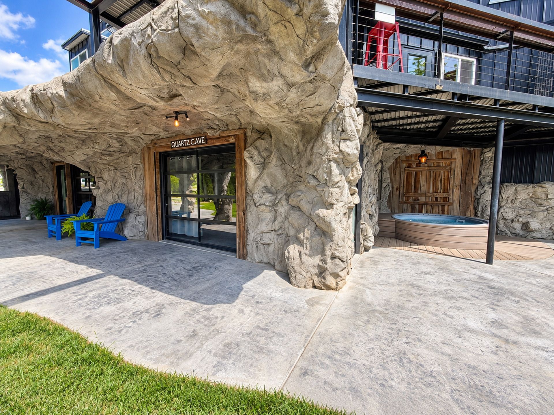 A building with a rock-like facade, a door labeled 'QUARTZ CAVE,' blue chairs outside, and a hot tub area.