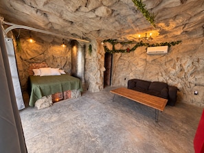 Une pièce comprenant un lit, un banc, un canapé et un mur dont la texture imite celle de la roche.