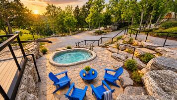 A hot tub surrounded by blue chairs and a stone deck, with a wooden deck and railing on the left.
