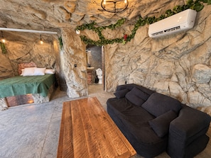 Une pièce comprenant un lit, un canapé, une table en bois et une salle de bain avec un mur en briques.
