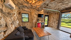 Quarto com parede de pedra, TV de tela plana acima de um eletrodoméstico vermelho, mesa de madeira e sofá seccional.
