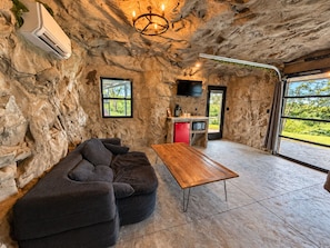 Una habitación con pared de piedra, un televisor de pantalla plana montado sobre un electrodoméstico rojo, una mesa de madera y un sofá seccional.