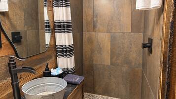 A bathroom with a wooden vanity, a large basin, a shower with a black faucet, and a mirror.