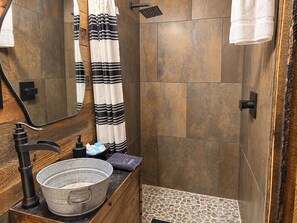Un baño con tocador de madera, un lavamanos grande, una ducha con grifo negro y un espejo.