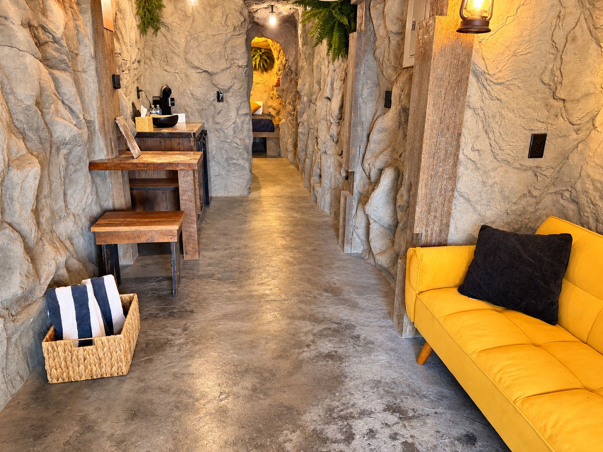 A spa room with a stone wall, a wooden bench, a yellow sofa, and a small table with a lamp.