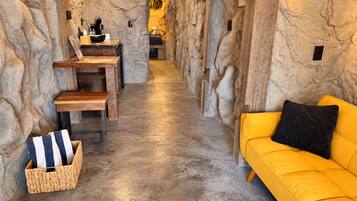 A spa room with a stone wall, a wooden bench, a yellow sofa, and a small table with a lamp.