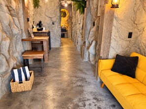 Un cuarto de spa con pared de piedra, un banco de madera, un sofá amarillo y una pequeña mesa con una lámpara.