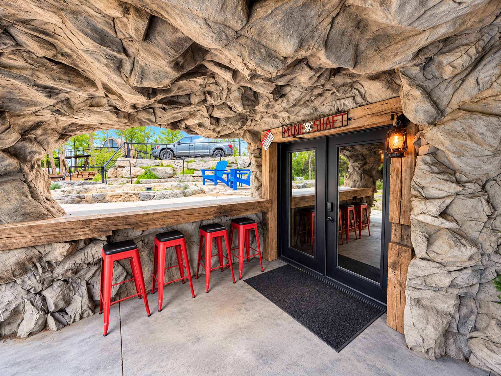 An interior bar area with a stone wall backdrop, bar stools, and a view of a parked vehicle outside.