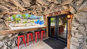 An interior bar area with a stone wall backdrop, bar stools, and a view of a parked vehicle outside.