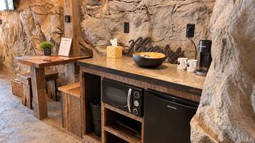 Una cocina con un fondo de pared de piedra, una mesa de madera, un tazón, una cafetera y un microondas.