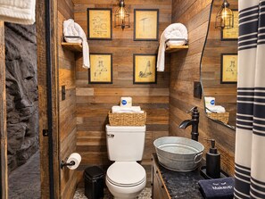 Un baño con paredes de madera, planos enmarcados, inodoro, lavamanos y toallas en estantes.
