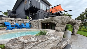Edifício moderno com área de piscina, cadeiras azuis e pedras grandes.
