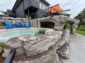Un edificio moderno con zona de piscina, sillas azules y rocas grandes.