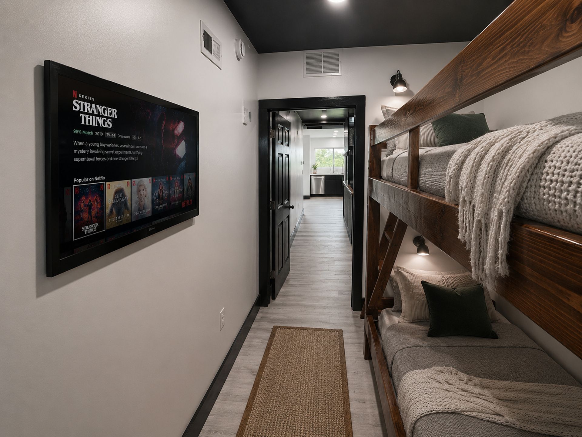 A hallway with a bunk bed, a TV displaying 'Stranger Things', and a kitchen in the background.