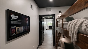 Un corridoio con un letto a castello, una TV che mostra 'Stranger Things' e una cucina sullo sfondo.