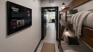 A hallway with a bunk bed, a TV displaying 'Stranger Things', and a kitchen in the background.