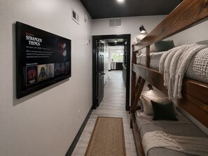 A hallway with a bunk bed, a TV displaying 'Stranger Things', and a kitchen in the background. - Altura Tower - With a View (Lancaster)