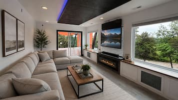 A modern living room with a sectional sofa, a fireplace, and a large window with a view of greenery.