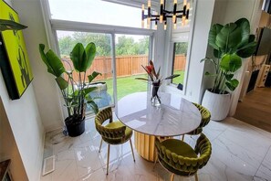 A dining area with a round table and chairs, surrounded by large potted plants, and a view of a backyard through a glass door. - Luxury Oakville Home | 4BR | Contemporary Design (Oakville)