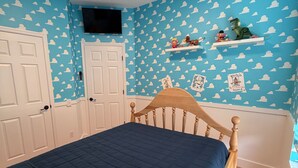 Une chambre à coucher avec un lit, des portes blanches, un téléviseur fixé au mur et un mur décoré de motifs nuageux.