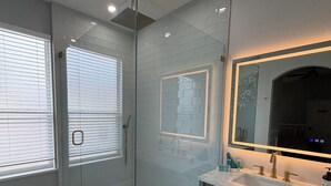 Une salle de bain moderne avec une douche à parois de verre, un meuble-lavabo doté d’un grand miroir et un sol carrelé.