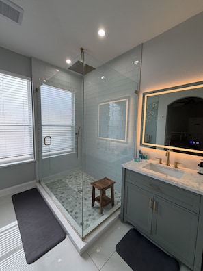 A modern bathroom with a glass-enclosed shower, a vanity with a large mirror, and a tiled floor. - Unique Home Gated Community Heated Pool 5 miles to Disney (Kissimmee)