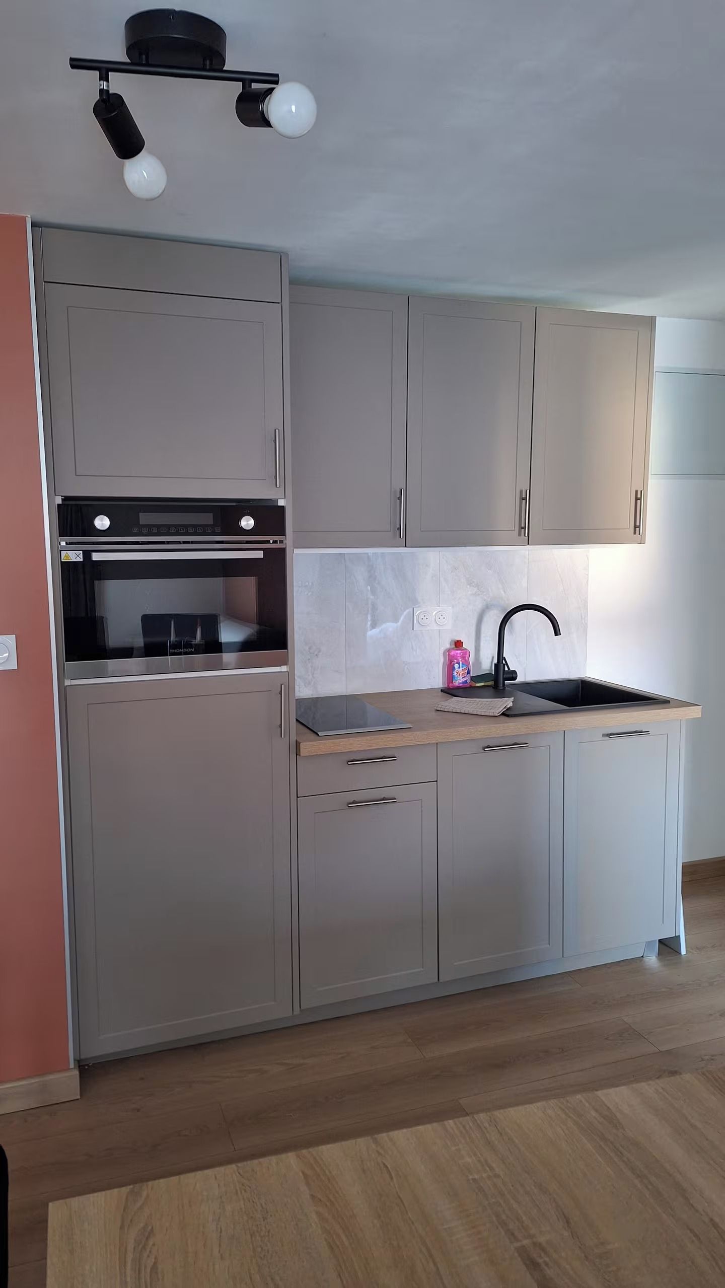Een keuken met grijze kastjes, een zwarte oven, een spoelbak en een houten aanrecht.