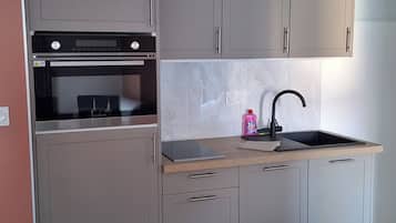 Een keuken met grijze kastjes, een zwarte oven, een spoelbak en een houten aanrecht.