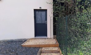 Una puerta negra con un pequeño escalón que la precede, rodeada de grava y un borde de madera.