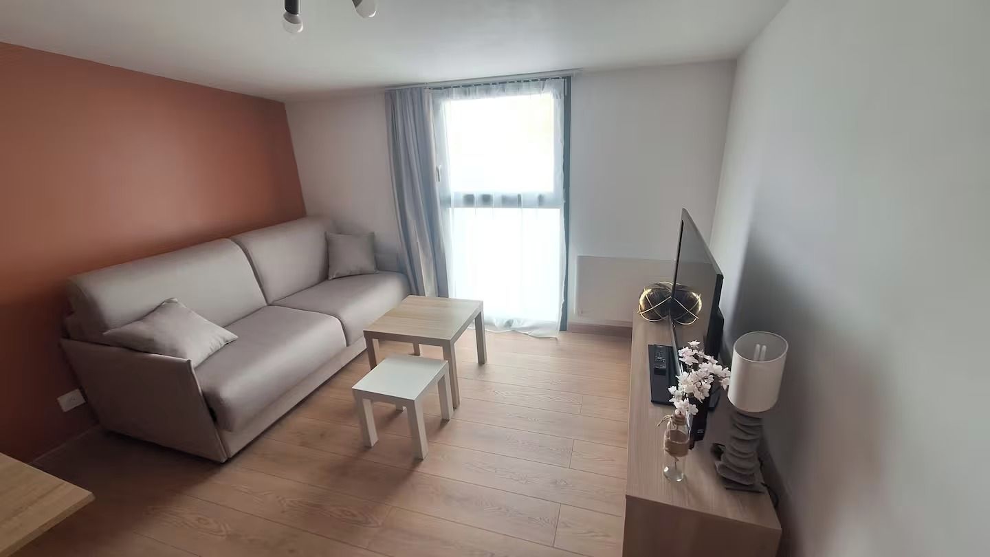 Een moderne woonkamer met een bank, een salontafel, een tv-meubel en een raam met gordijnen.