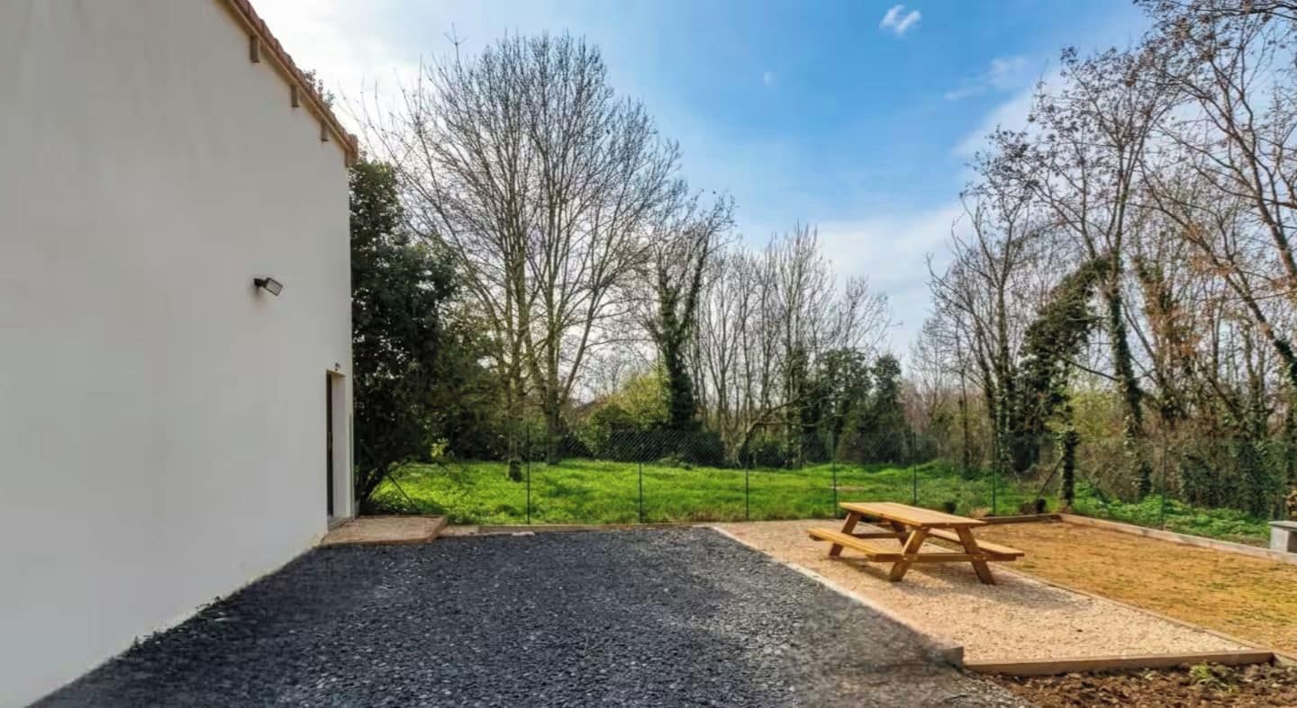 Een picknicktafel in een grasveld, met een kiezelpad dat naar een wit gebouw leidt.