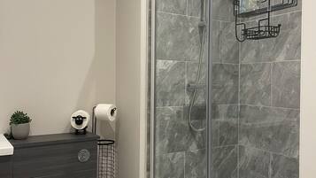 Een moderne badkamer met een glazen douchecabine, marmeren tegels, een toilet, een wastafel met een plant en een toiletrolhouder.
