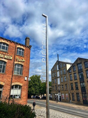 Een straatbeeld met een gebouw van baksteen, waarop 'The Piece Hall' staat, en een moderne straatlantaarn.