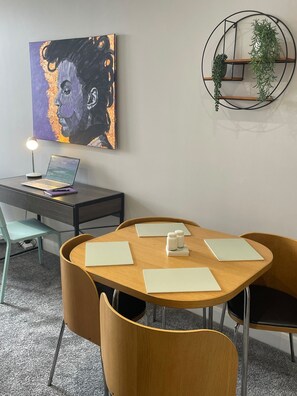 Un espacio de oficina moderno con una mesa redonda, dos sillas, un escritorio con una computadora portátil, un cuadro y una planta colgante en la pared.