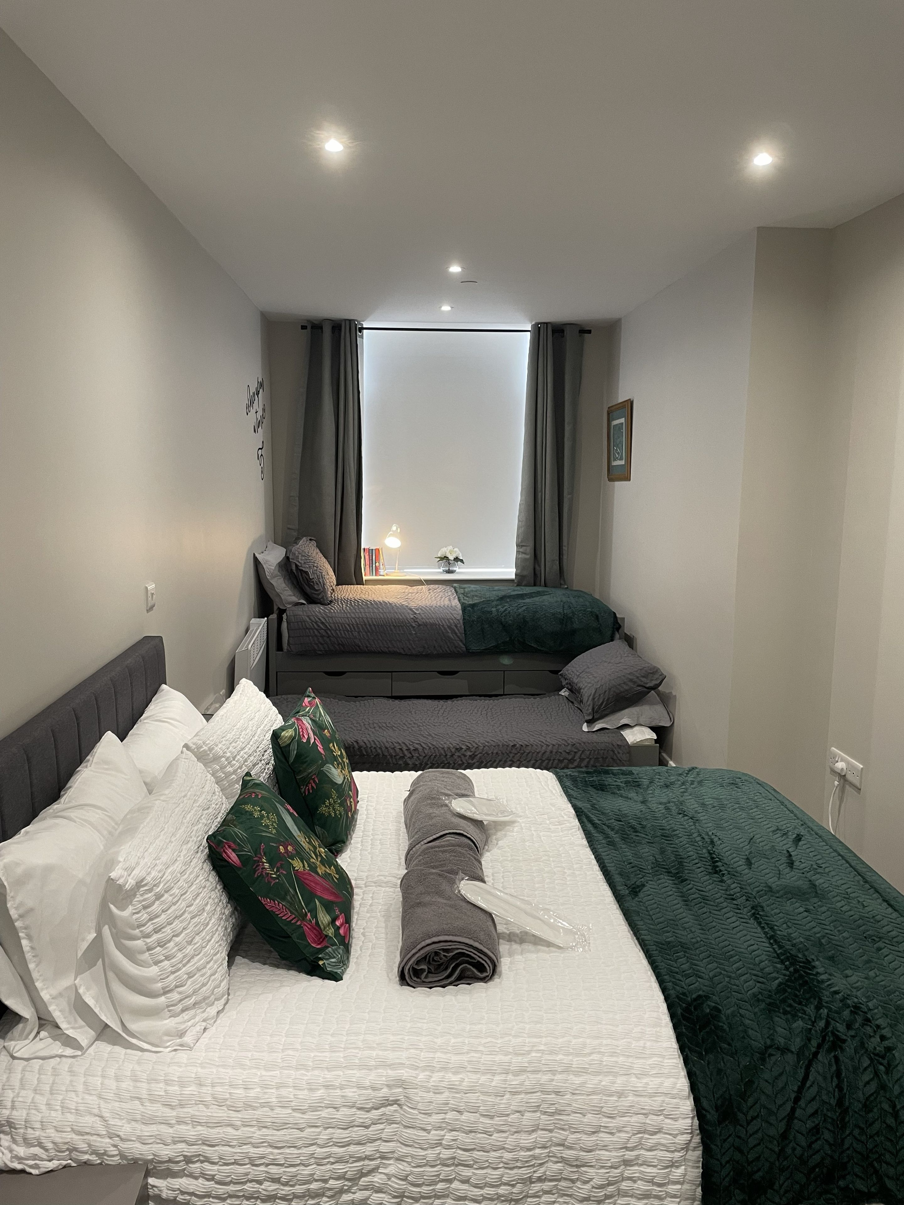 A bedroom with a bed, a window with curtains, a bedside table with a lamp, and a wall-mounted picture.