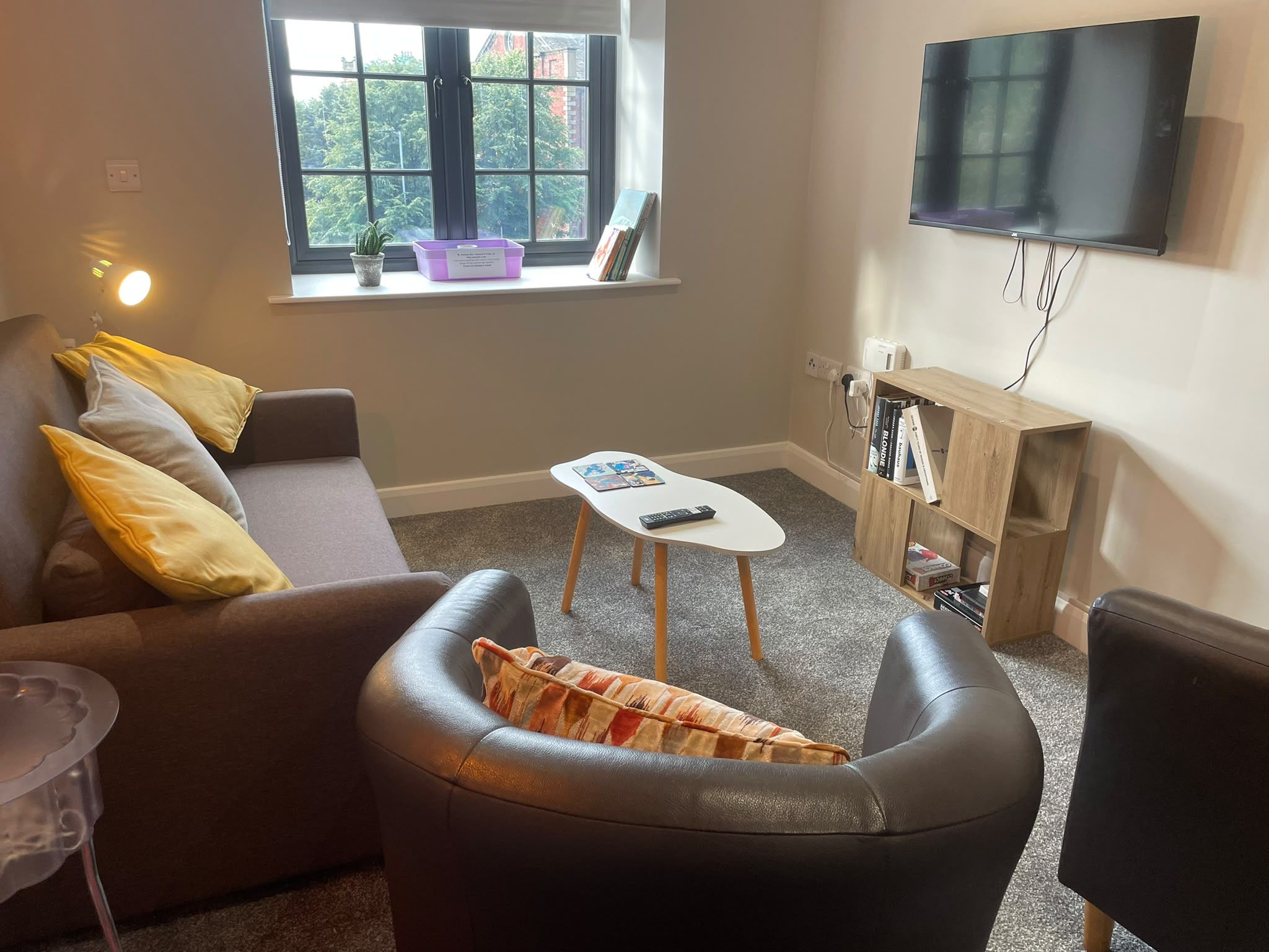 Een woonkamer met een bank, een bijzettafeltje, een televisie en een boekenkast.