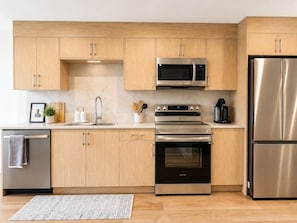 A modern kitchen with stainless steel appliances, wooden cabinets, and a tiled backsplash. - Westshore Oasis | 1-Bedroom Victoria Retreat (Victoria)