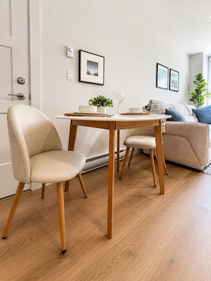 A modern living room with a wooden dining table, two chairs, a sofa, and a small side table. - Westshore Oasis | 1-Bedroom Victoria Retreat (Victoria)