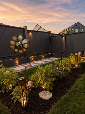 Ein Garten mit einer verzierten Metallblume, einem Kiesweg und einem Zaun.