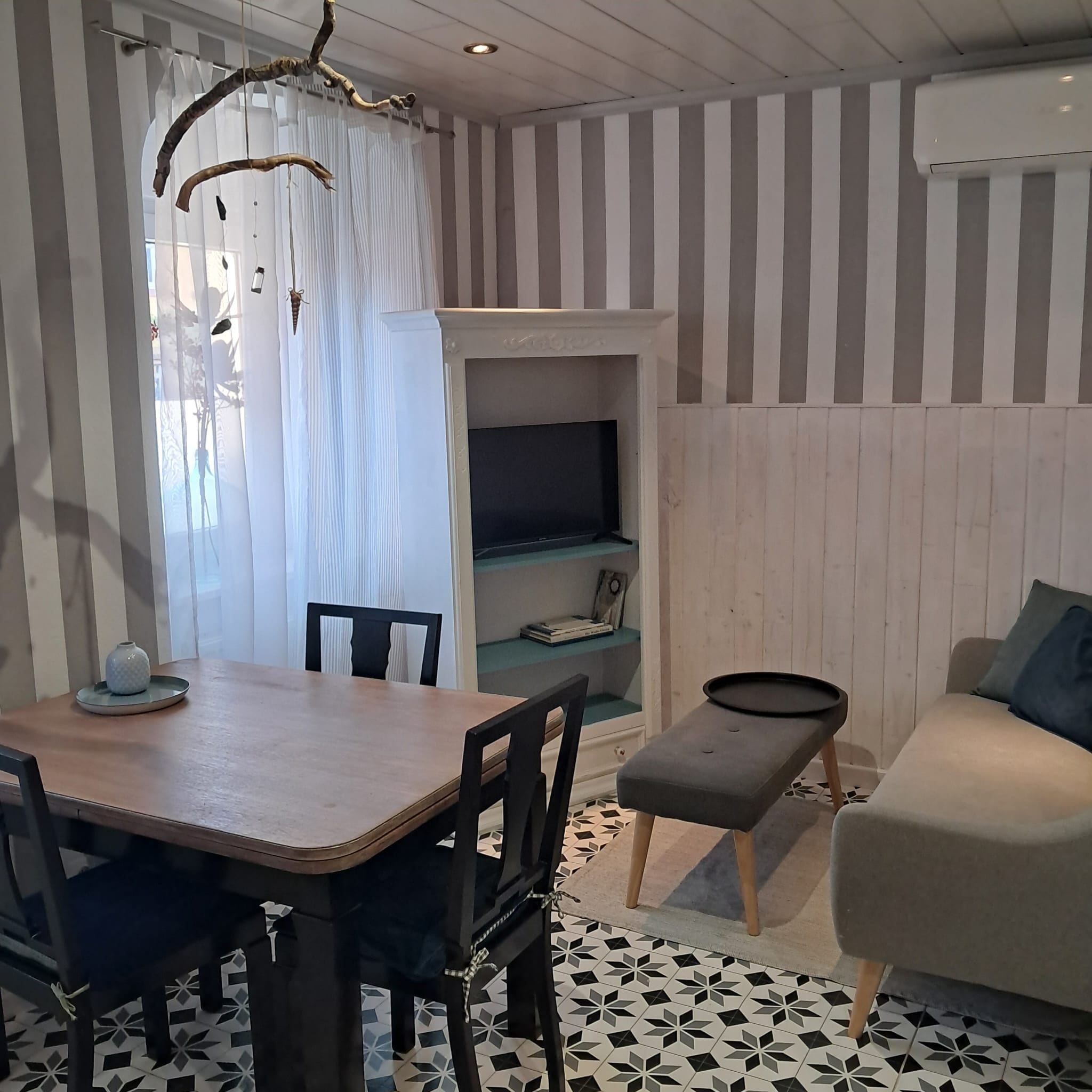 A room with a dining table, chairs, a sofa, a TV, and a patterned floor.